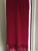 Full length view of a burgundy fuchsia alpaca scarf hanging, showing fringe on both ends.