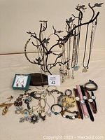 Jewelry stand displaying necklaces with assorted costume jewelry including rings, bracelets, brooches, watches, and earrings arranged below it.
