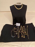 Full view of assorted gold-tone costume jewelry on black fabric and black bust showing necklaces and bracelet