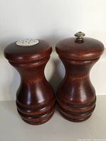 Front view of the solid maple pepper grinder and salt shaker set with the salt shaker showing multiple holes on top and the pepper grinder with a turning knob.