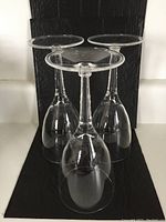 Photo showing three clear plastic wine glasses upside down highlighting the bowl and stem shape with a black background