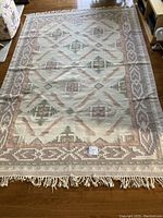 Full view of the 6x9 ft duhurrie rug with geometric tribal patterns and fringe on wooden floor
