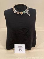 Neutral background showing full front view of necklace on a display bust, highlighting the overall shape and placement of decorative elements.