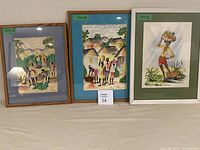Three framed Jamaican paintings depicting different scenes of village life, two portraits of groups of people, and one character with basket on head.