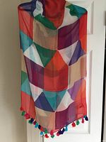 Multicolor geometric patterned scarf hanging against a white door, showing full length and colorful fringe edges.
