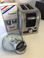 Photo shows Moulinex chopper with original box, Oster 2-slice toaster, and Trudeau kitchen scale placed in front. Clear view of box graphics and toaster controls.