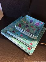 Melamine dish set stacked showing tropical floral design on square plates and bowls.