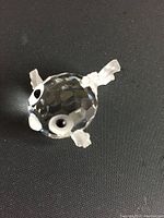 Close-up photo of small Swarovski crystal figurine shaped as a glow fish on a dark background. Shows faceted crystal body and detailed eyes and fins.