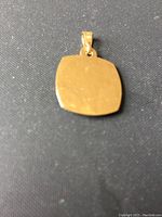 Top view of the back of the square gold pendant, smooth polished surface, showing the bail for hanging.