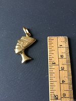 Front view of Nefertiti gold medallion next to ruler indicating about 1 inch size