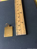 Photo of the back side of the square 18K gold medallion next to a ruler showing size.