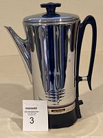 Front side view of the vintage stainless steel coffee percolator showing polished body, black handle, lid with knob, and base with branding.