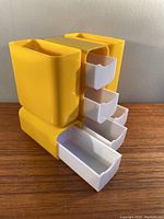 Front angle showing yellow plastic desk organizer with three white drawers extended