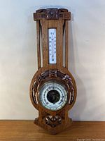 Full view of antique wooden weather station with thermometer and barometer in carved oak frame
