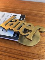 Brass clip shaped as the word 'Later' placed on a wooden surface, holding a book.