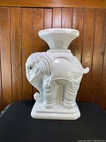 Side view of white ceramic elephant accent table with detailed features and painted eyes, showing general condition and shape