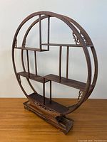 Three images showing different angles of a round, carved wooden display shelf with multiple compartments and a carved rectangular base.