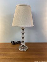 Front view of the assembled Hollywood Regency cut glass lamp with beige tweed lampshade on a wooden surface under neutral lighting.