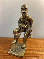 Front view of brass miner figurine showing detailed facial features, attire, and shovel resting on the base.