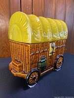 Side front view showing the detailed wooden wagon with barrel, wheels and door latch, yellow covered top with ridges.