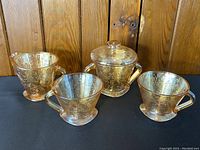 Jeanette Floragold carnival glass creamer, sugar bowl with lid, and two teacups displayed against wood background
