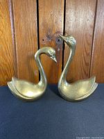 Clear front view of the pair of brass swan figurines showing their size difference and curved necks.