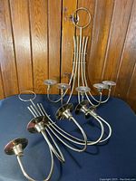 Two brass candle holders placed on fabric surface, close-up from side and top angles revealing the individual candle cups and arms.