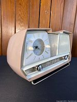 Angled left-front view showing pink bakelite case, analog clock face, speaker grille and chrome knobs