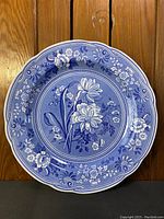 Front view showing detailed blue and white floral botanical design with scalloped edge on the ceramic plate
