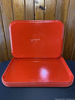 Stack of six red fibreglass lunch trays showing top tray surface and thickness of set