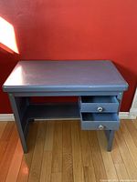 Front view of a compact gray metal desk with two drawers open, showing wear and some rust spots.