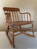 Side angle view of the small wooden rocking chair showing the turned spindle back, curved armrests, and rocker base.