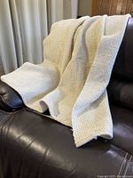 Beige wool tweed blanket draped on brown leather chair showing texture and weight.