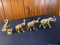 Side view of four brass elephant figurines, showing varied poses and detailed engravings, one with trunk up acting as bottle opener