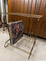 Angle showing the side and front view of vintage brass record stand holding vinyl records on bottom rack.