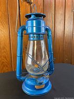 Front view of blue metal Dietz No 20 lantern showing glass globe, metal wire guard, wick and base with label.