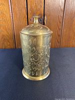 Front and side view of cylindrical brass jar with floral and leaf etched designs, featuring the lid with knob handle