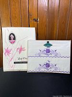 Two white pillow cases with purple floral embroidery displayed on a wooden door with the original packaging box visible