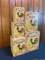 Five vintage wooden stacking canisters with rooster designs labeled Tea, Coffee, Sugar, Flour, Cookies stacked and grouped