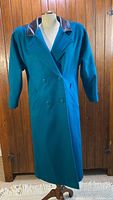 Full front view of vintage long teal wool coat with leather collar and shoulder accents on mannequin.