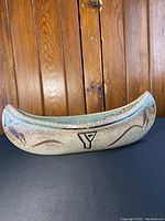 Photo of ceramic canoe sculpture showing YMCA logo and bird motifs on exterior side.