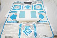 Photo of Dance Dance Revolution accessory mat laid flat showing blue and white directional arrows and Konami and Wii branding.