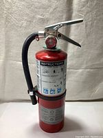 Photo of a red 5-pound ABC dry chemical fire extinguisher with operating handle, pressure gauge, black hose, and printed instructions label.