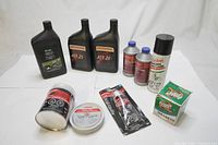 Photo showing all items in the lot arranged on a white surface including engine oil, transmission fluid bottles, brake fluid, body filler containers, aerosol spray, and oil filter.