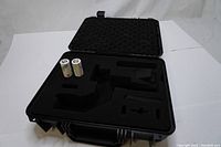 Open black protective hard case with foam insert custom-cut to hold camera stabilizer equipment and accessories. Two white cylindrical batteries are positioned vertically in one section of foam.