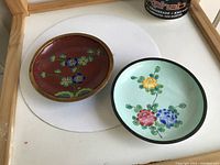 Two small Chinese cloisonne bowls showing front with floral decoration, one reddish-brown and one light green