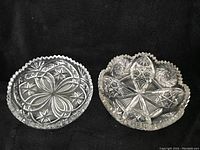 Two heavy crystal candy dishes displayed on black cloth, showing intricate cut patterns and scalloped edges.