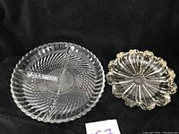 Two heavy crystal candy dishes on black background. Large dish has three sections divided by internal walls and spiral cut pattern on base with scalloped edge. Smaller dish has scalloped petal edge and starburst cut pattern.