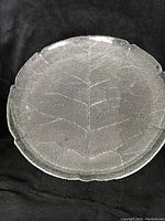 Top-down view of clear glass plate showing detailed leaf vein pattern across the entire surface. Plate appears round with leaf-shaped edge.