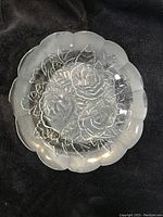 Top view of clear glass serving plate showing embossed three roses and leafy pattern with scalloped edges on black background.